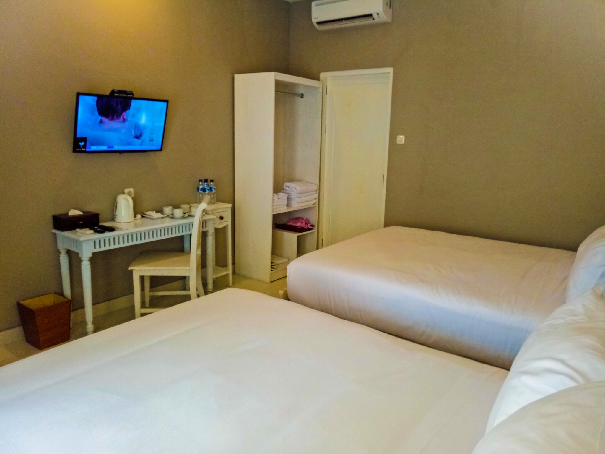 Habitación de hotel con dos camas, un escritorio con silla, televisión montada en la pared y un armario.