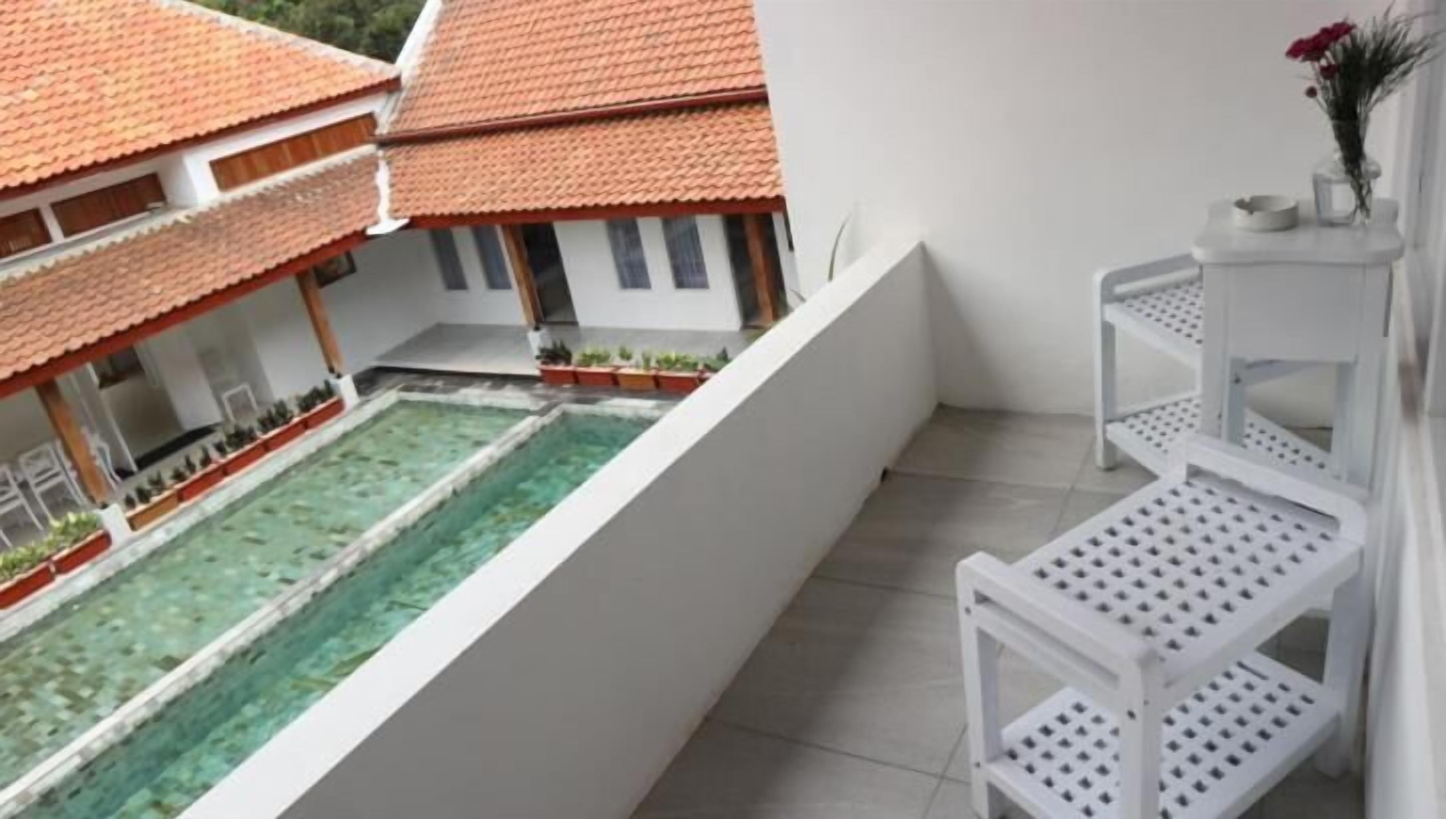 Un balcone con piscina, mobili bianchi e vista su un edificio tradizionale con tetto in tegole.