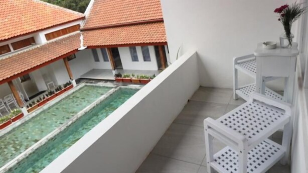 A balcony with a pool, white furniture, and a view of a traditional building with a tiled roof. - Sinom Borobudur Hotel (Borobudur)