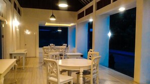 Un espace repas avec des tables et des chaises rondes, un plancher en bois et de grandes fenêtres.