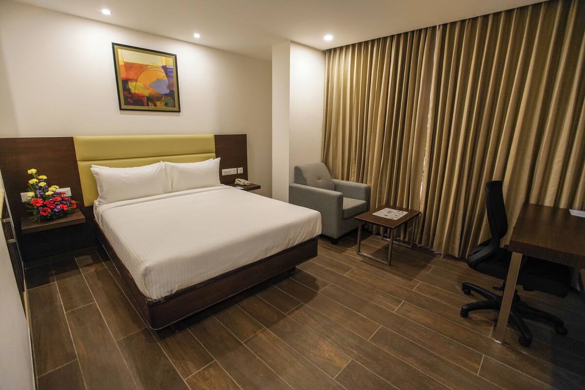 A hotel room with a large bed, a desk, a chair, and a curtain.