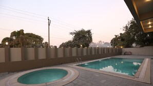 Una piscina con un jacuzzi, rodeada por un muro bajo y una terraza con baldosas.