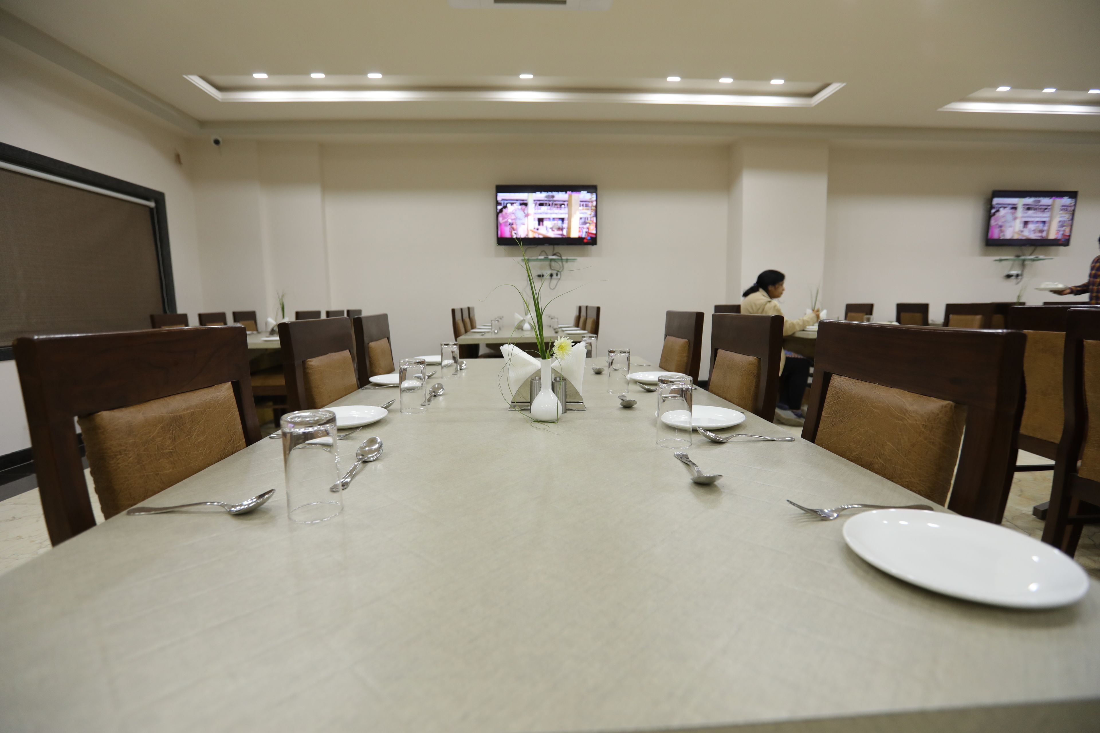 A conference room with a long table set for a meeting, equipped with chairs, a TV screen, and a floral centerpiece.
