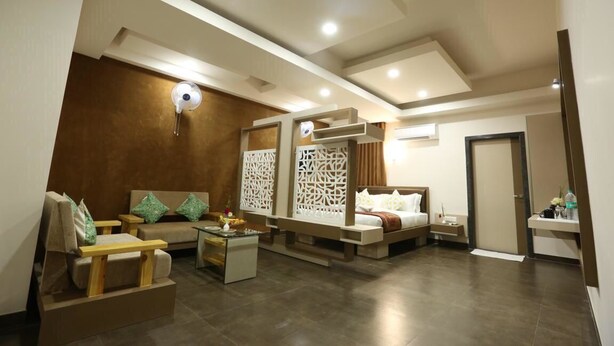 A modern hotel room with a sofa, a bed, a small table, and a decorative partition. - Kukda Resort Chittorgarh (Chittorgarh)