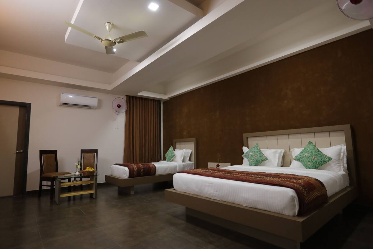 A hotel room with two beds, a ceiling fan, an air conditioning unit, and a large window with curtains.