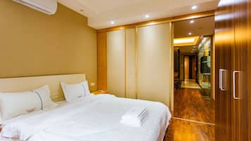 Une chambre d’hôtel avec un lit, du linge de lit blanc, une armoire en bois et un couloir menant à la salle de bain.
