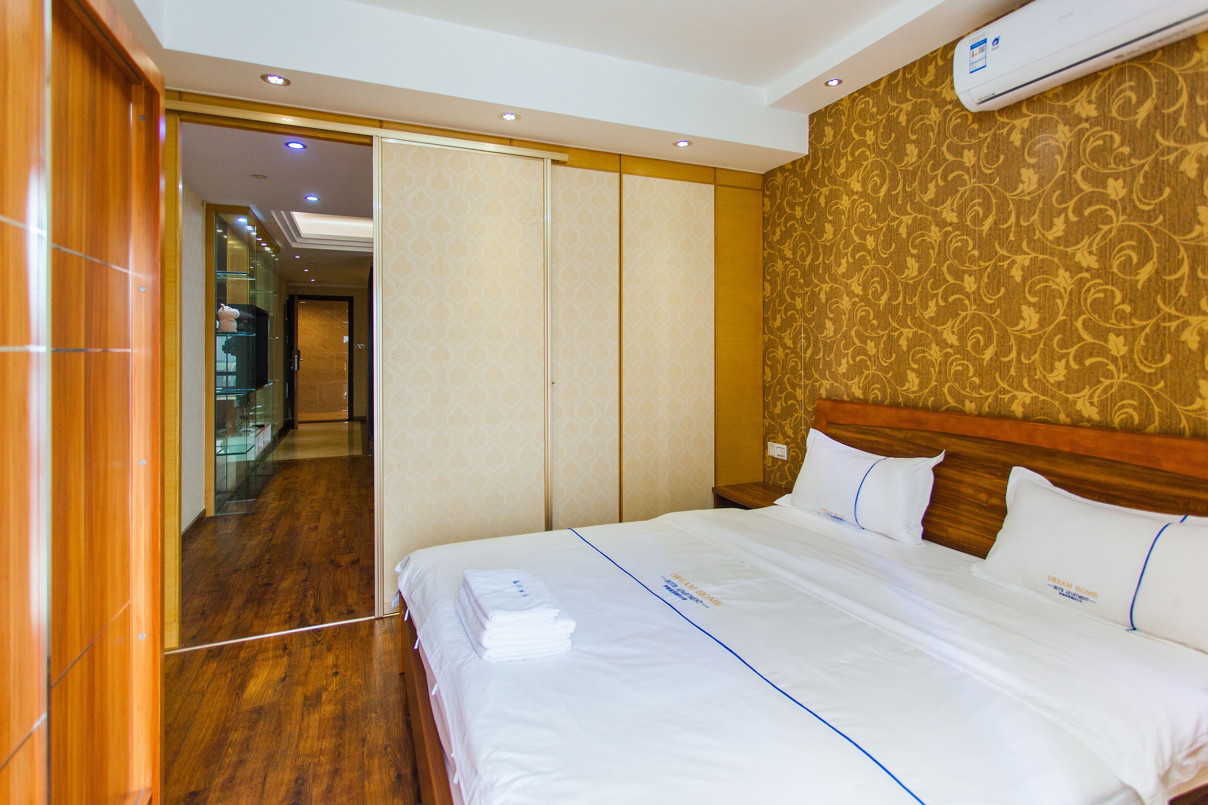 A hotel room with a neatly made bed, a wooden floor, and a patterned wallpaper on the wall.