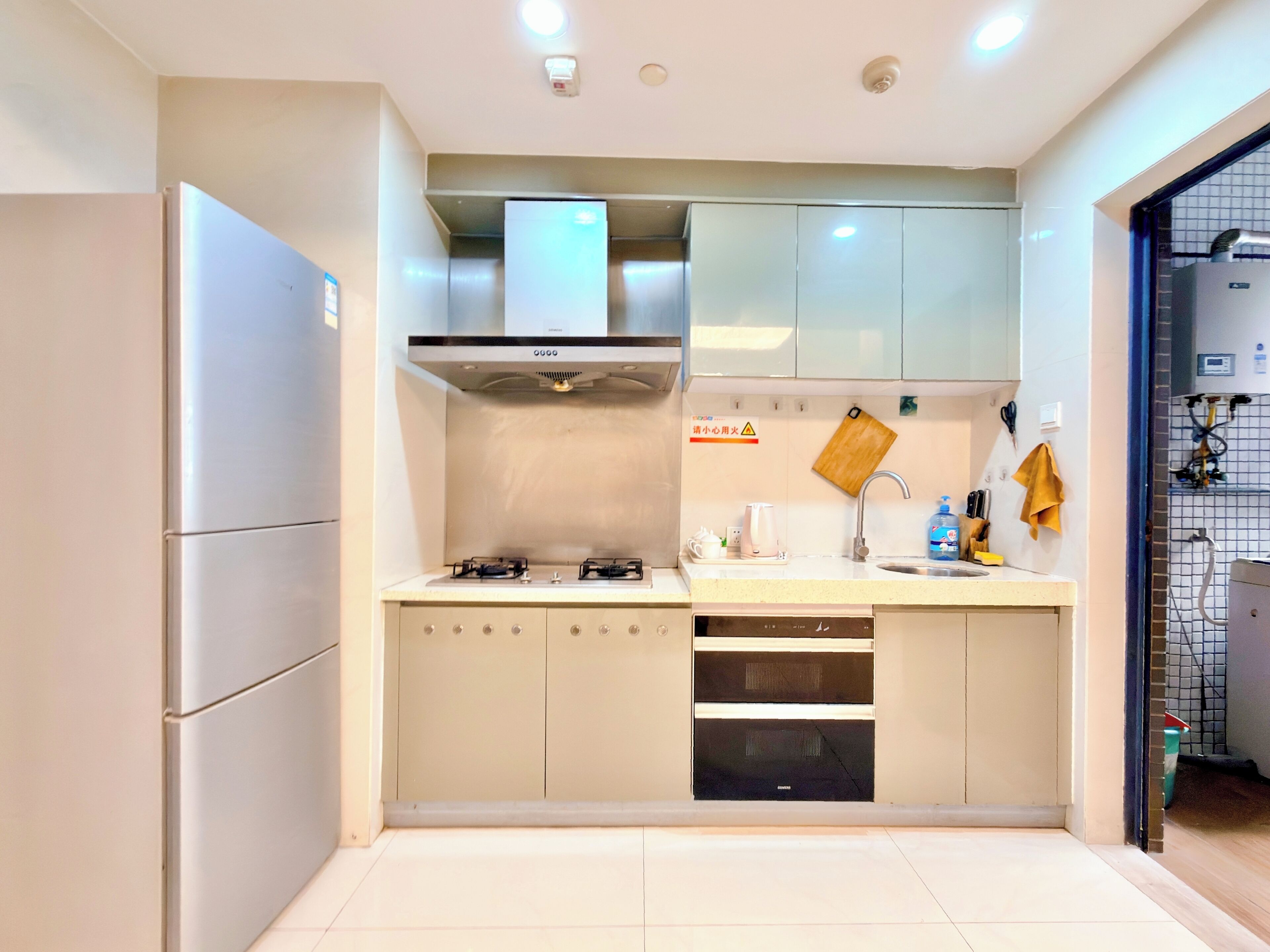 A compact kitchen with a built-in gas stove, a stainless steel refrigerator, and a microwave.