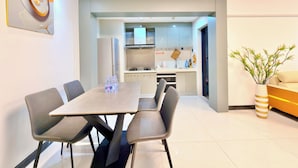 Un soggiorno moderno con tavolo da pranzo, sedie, divano, cucina con mobili ed elettrodomestici, e una pianta decorativa.