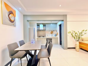 A modern living room with a dining table, chairs, a sofa, a kitchen with cabinets and appliances, and a decorative plant. - Yujia Aparthotel - Zhongshan Lihe Square Branch (Zhongshan)