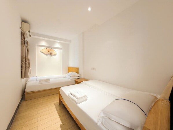 A hotel room with two beds, wooden flooring, a wall-mounted air conditioner, and a decorative wall piece.