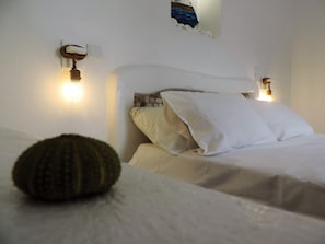 A bed with white bedding and a single green pillow, two wall-mounted light fixtures, and a small wall-mounted switch.