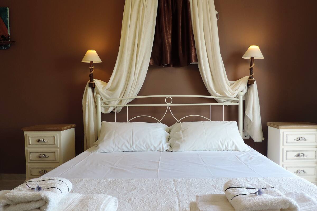 Una cama bien hecha con sábanas blancas, dos mesitas de noche con lámparas y un dosel sobre la cama.