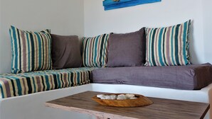 Un canapé d’angle avec des coussins à rayures, une table d’appoint en bois sur laquelle repose un bol rempli de pierres décoratives, et une œuvre d’art murale en bois de couleur bleue.