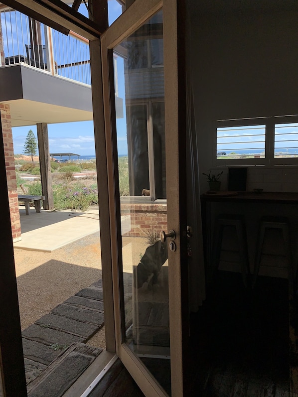 Una puerta de cristal da a un patio exterior con vistas al océano y un camino de piedra.