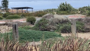 A park with a wooden fence, various shrubs, and a covered structure. - Amazing Ocean Front Studio - Sunsets, Breakfast, Water  (Port Noarlunga South)