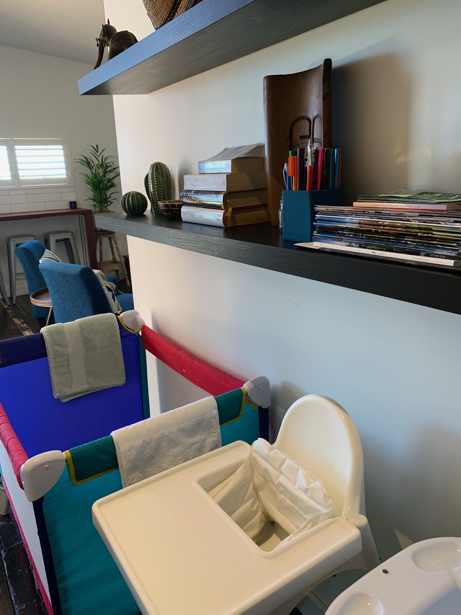 Um quarto com uma cadeira azul, uma cadeira branca e uma mesa pequena. Há uma estante com livros e um cacto.