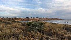 A coastal landscape with a sandy beach, grassy dunes, and a cliff with buildings. - Amazing Ocean Front Studio - Sunsets, Breakfast, Water  (Port Noarlunga South)