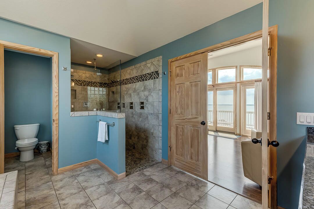 A bathroom with a shower, toilet, and a large wooden door leading to a balcony.