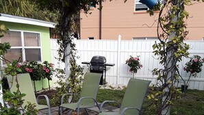 A patio area with a glass table, two green chairs, a grill, and a decorative plant. - Guest House  1Bedroom Sleeps 4 (Cocoa Beach)
