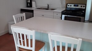 A kitchen with white cabinets, a stainless steel sink, a stove, and two white chairs with wooden seats. - Guest House  1Bedroom Sleeps 4 (Cocoa Beach)