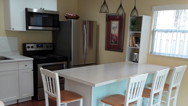 A modern kitchen with white cabinetry, stainless steel appliances, and a central island with bar stools. - Guest House  1Bedroom Sleeps 4 (Cocoa Beach)