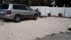 A silver SUV parked on a gravel driveway with a white fence and potted plants in the background. - Guest House  1Bedroom Sleeps 4 (Cocoa Beach)