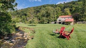 A house with a red roof, a grassy yard, and a stream. - Charming Cottage in the Village of Warm Springs with Warm Thermal Spring (Warm Springs)