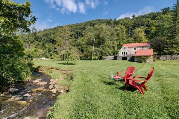A house with a red roof, a grassy yard, and a stream.