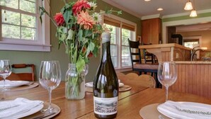 A dining table set with wine glasses, a bottle of wine, and a vase of flowers. - Charming Cottage in the Village of Warm Springs with Warm Thermal Spring (Warm Springs)