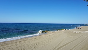 Une plage avec une eau d’un bleu limpide, un rivage sablonneux et quelques rochers.