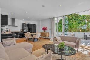 Ein moderner Wohnraum mit Küche, Essbereich und großem Fenster mit Blick auf Grünflächen.