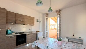 A modern kitchen with wooden cabinets, a gas stove, and a sink. There is a dining table with a floral tablecloth and a potted plant. - Il giardino (Piombino)