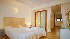 A hotel room with a large bed, a nightstand, a mirror, and a bathroom visible through a glass door.