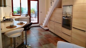 A modern kitchen with a central island, bar stools, a staircase, and a dining area with a view of the outdoors.