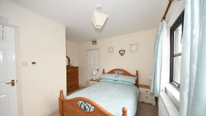 A bedroom with a wooden bed, a nightstand, a dresser, a radiator, and a window with curtains. - Self catering B&B or short holiday let (Saffron Walden)