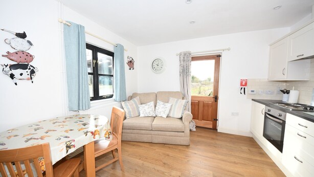 A kitchen with a dining area, wooden flooring, a sofa, and a clock on the wall. - Self catering B&B or short holiday let (Saffron Walden)