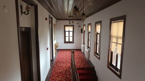 Un couloir avec un tapis rouge, des portes en bois et des fenêtres équipées de stores.