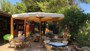 An outdoor patio with wicker tables and chairs, a large umbrella, and potted plants.
