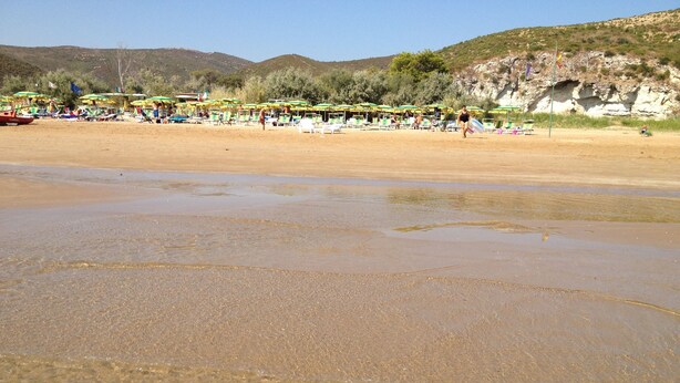 A beach with clear shallow waters, umbrellas, and people.