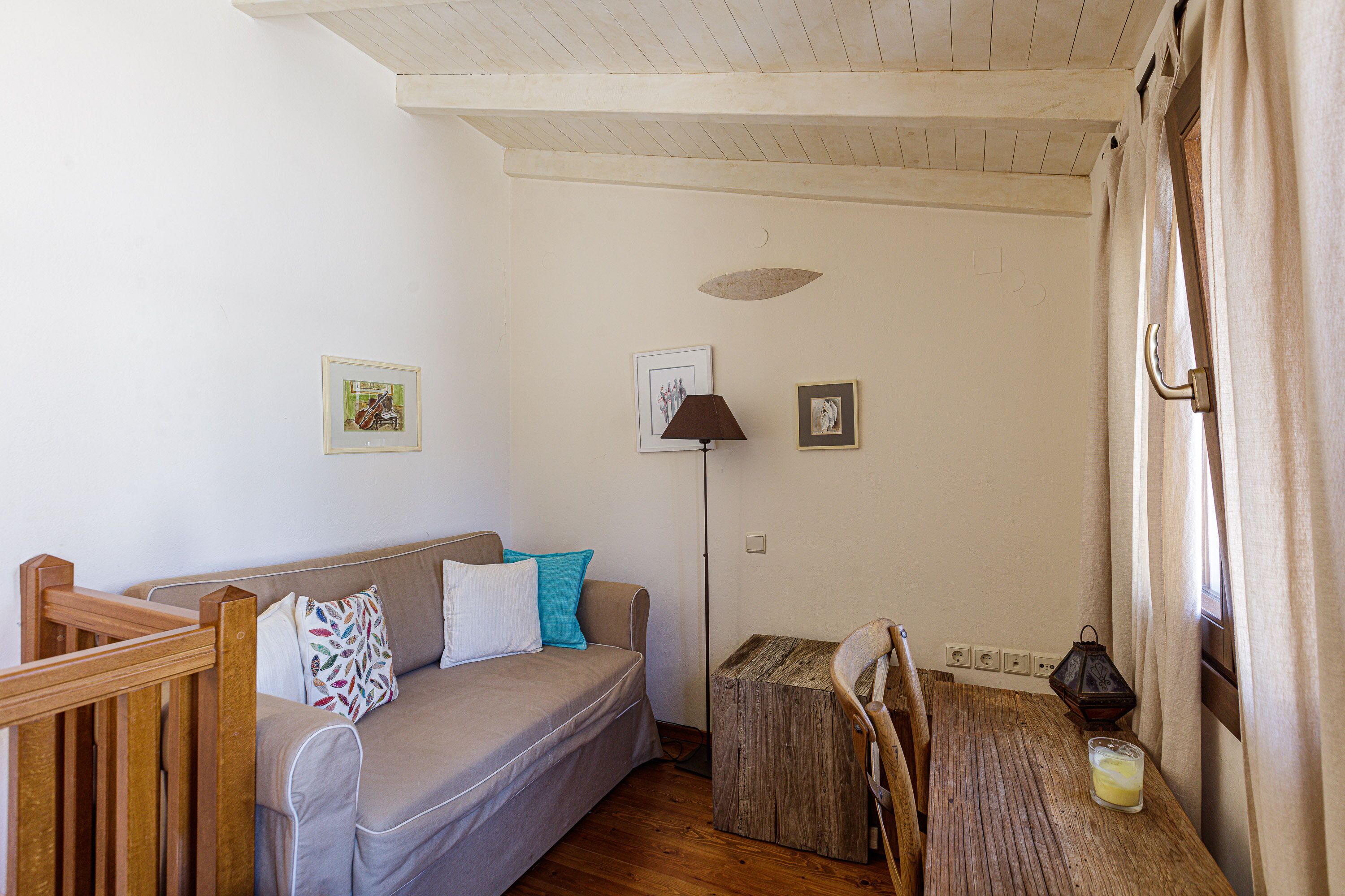 Una habitación acogedora con piso de madera, un sofá con cojines, una pequeña mesa de madera con un vaso y una lámpara de pie.