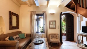 A cozy living room with a wooden coffee table, leather sofa, and a comfortable armchair. A ceiling fan and a wooden staircase are also visible. - Charming Venetian house in heart of Rethymno (Rethymno)
