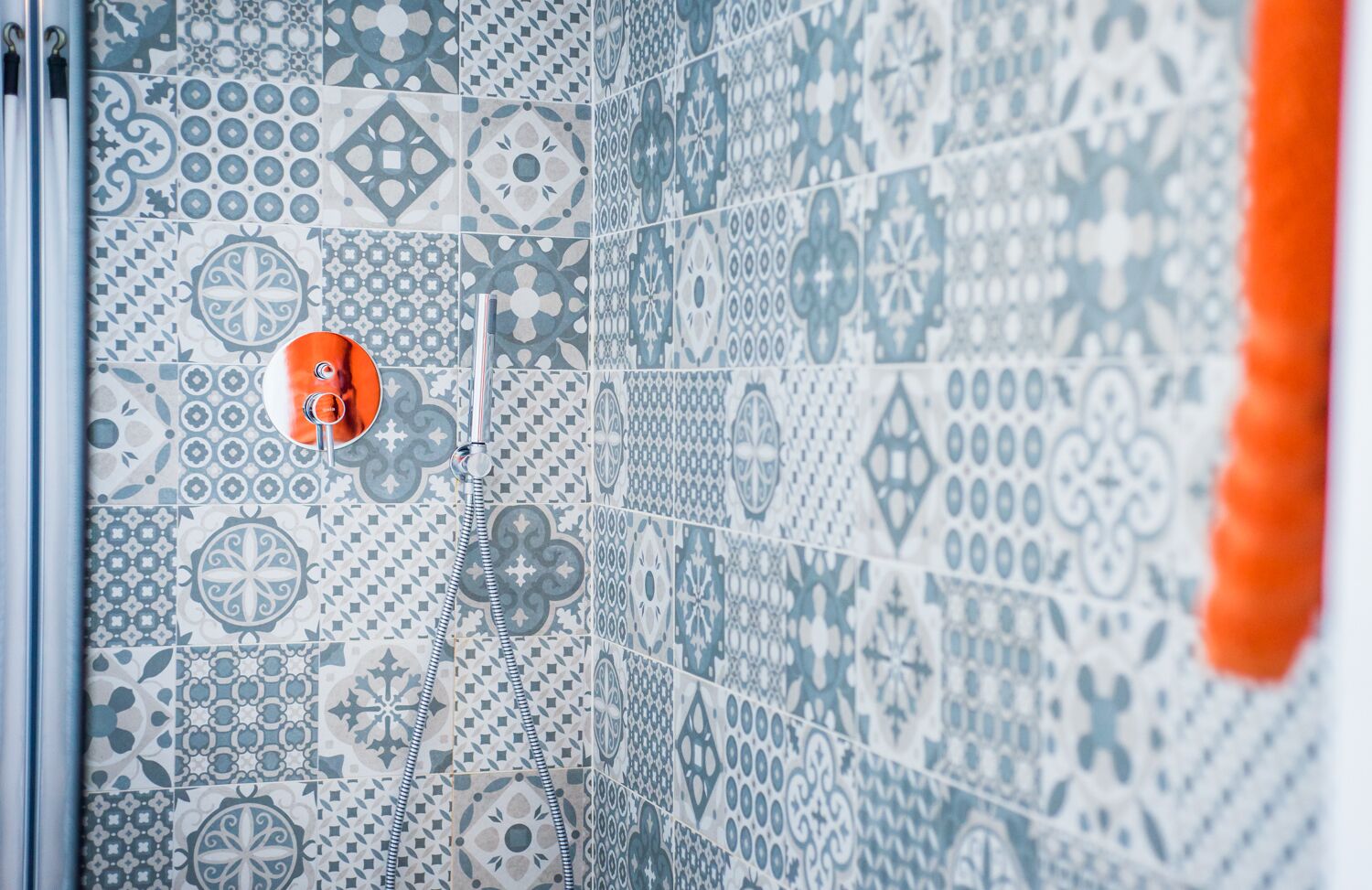 A bathroom with a shower area featuring a patterned tile wall and a visible shower head.