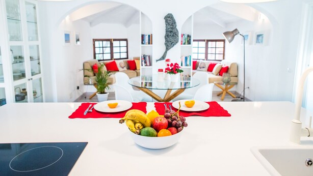 Une cuisine moderne dotée d’un îlot central, un coin repas avec une table en verre et un salon avec un canapé et une table basse.