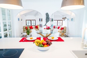 A modern kitchen with a central island, a dining area with a glass table, and a living room with a sofa and a coffee table.
