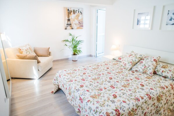 A bedroom with a floral bedspread, a sofa, a potted plant, and a painting of the Eiffel Tower.
