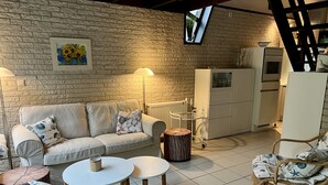 Een gezellige zithoek met een bakstenen muur, een bank, twee ronde tafels, een rieten stoel en een kast.