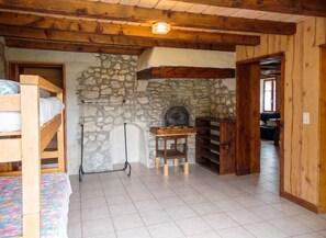 A rustic room with a stone wall, wooden beams, a bunk bed, a small table, and a fireplace. - Homerez - House in Septmoncel (Septmoncel)