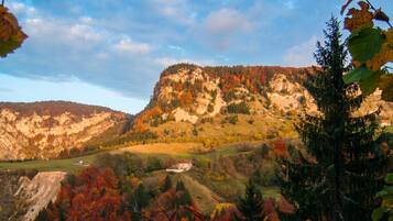 Paesaggio montano con fogliame autunnale, un piccolo edificio e cielo sereno.
