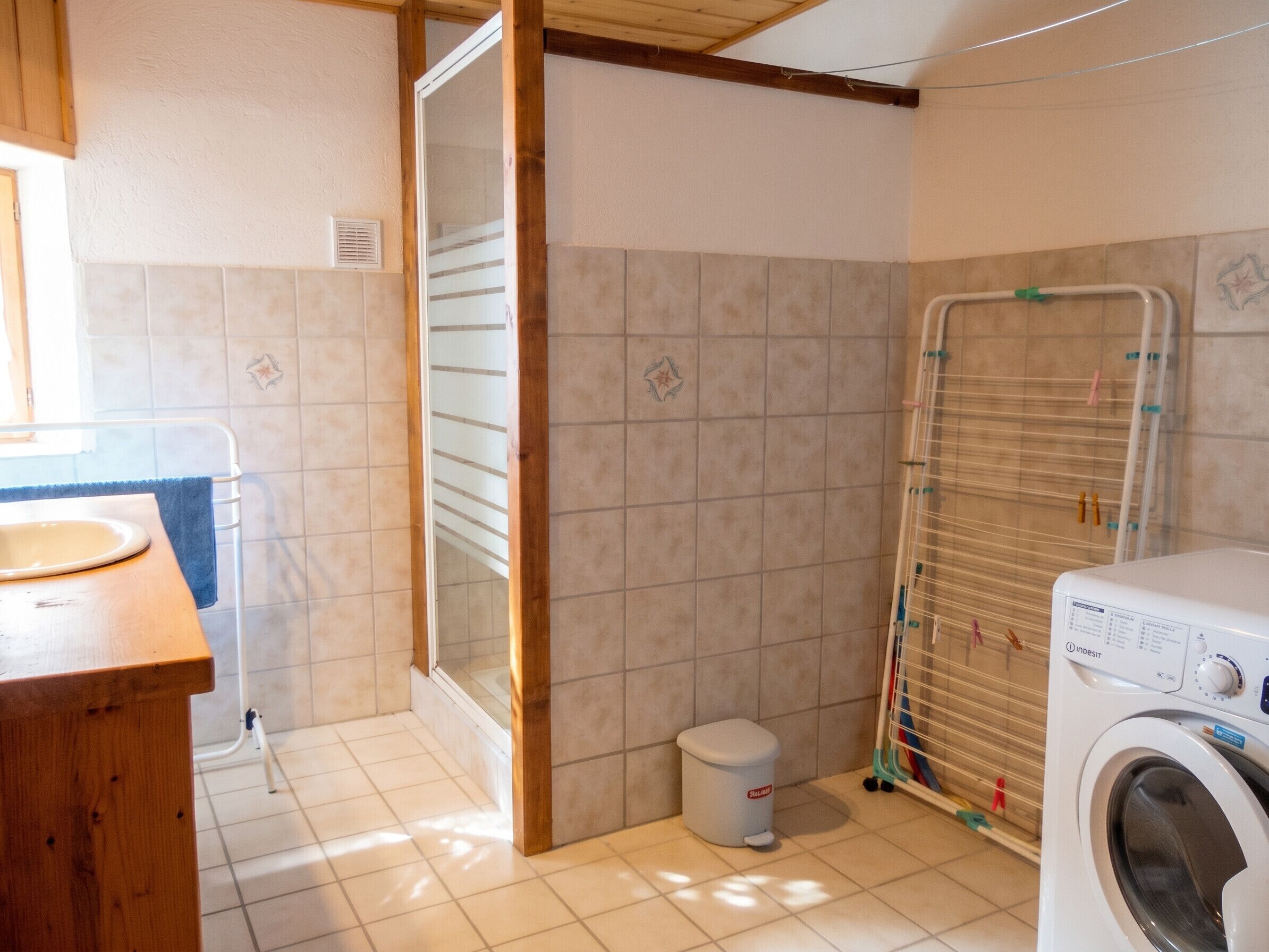 A bathroom with a washing machine, a small trash bin, and a towel rack.